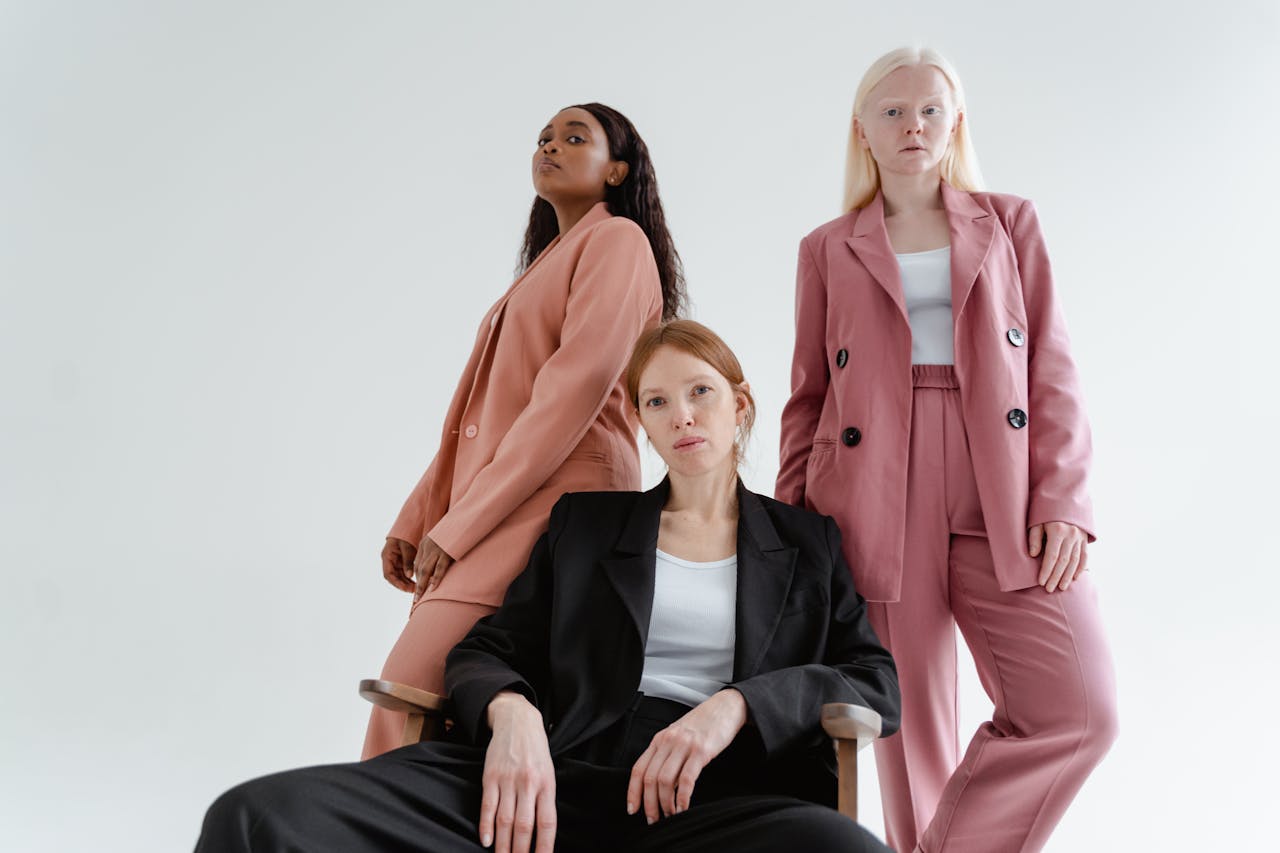 Three diverse women posing confidently in stylish blazers in a white studio setting.