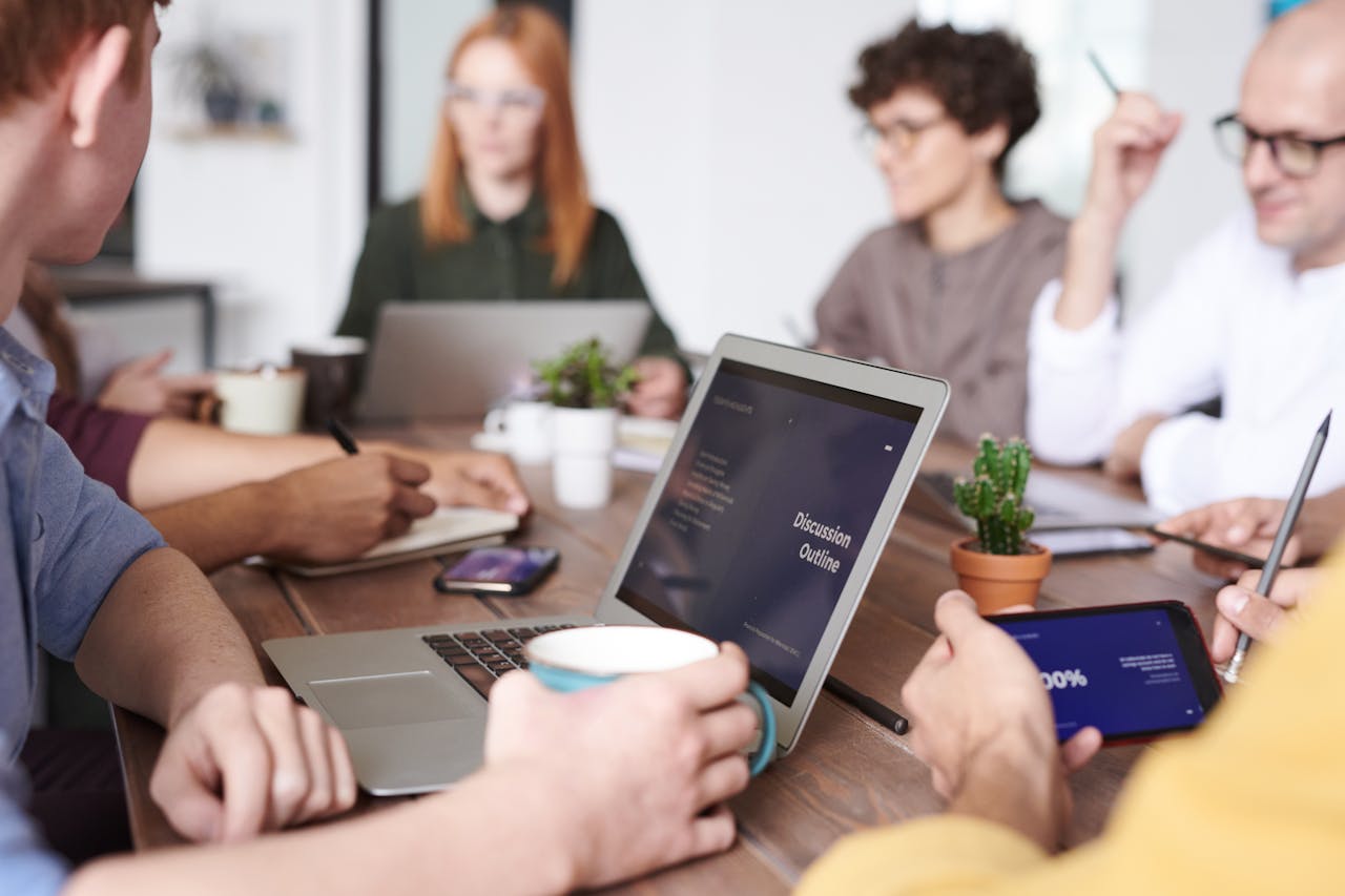 our-story-01 A diverse group of professionals collaborating with laptops and tablets in a modern office setting.