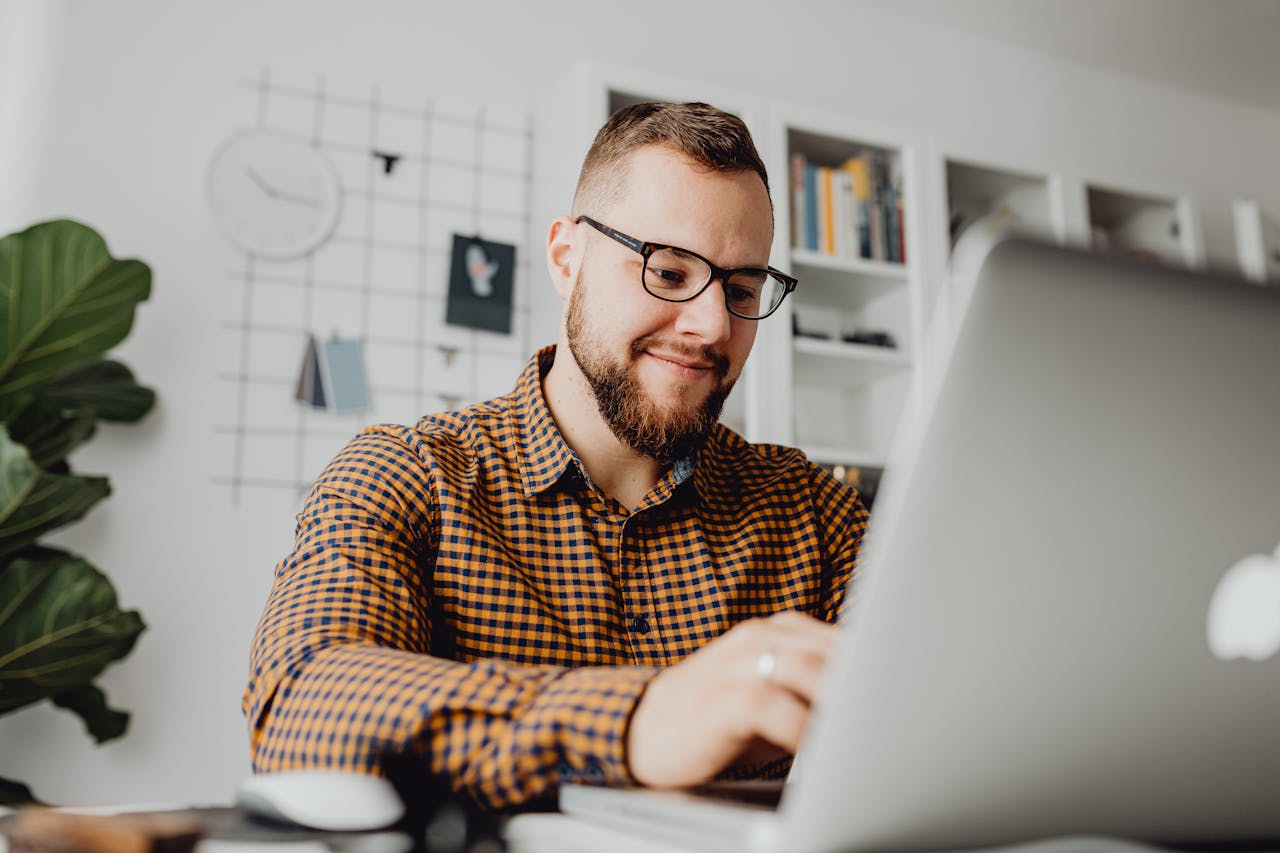 A confident man with glasses working on a laptop in a modern office setting.